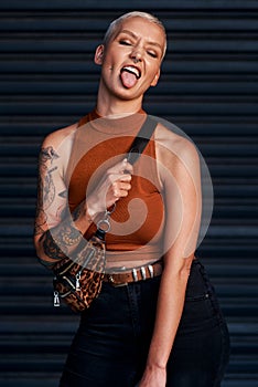 Im unapologetically me. an attractive young woman sticking out her tongue while standing against a dark background.