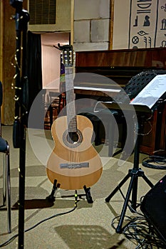 image of an acoustic guitar stands on stage near a music stand