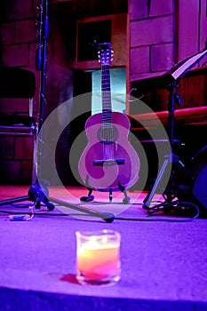 image of an acoustic guitar stands on stage near a music stand
