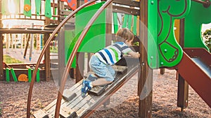 Photo of adorable toddler boy climbing and crawling on wooden staircase on children palyground at park photo