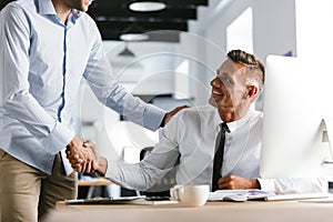 Image of adult businessmen coworkers 30s in formal clothes working in office, and shaking hands together