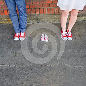 An image of adults in red sneakers next to baby pair of sneakers