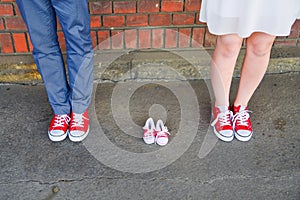 An image of adults in red sneakers next to baby pair of sneakers. Pregnancy and expectation concept.