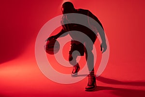 Image of african american basketball player bouncing basketball on neon red background