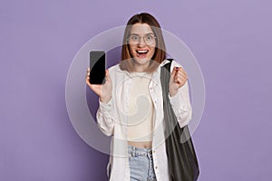 Image of amazed excited shocked woman wearing stylish clothing holding bag posing isolated over purple background, being surprised