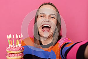 Image of amazed happy joyful woman with brown hair wearing stylish jumper, making point of view photo, rejoicing, holding donut