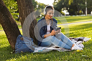 Beautiful young woman student in the park listening music with headphones using mobile phone.