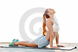 Beautiful young redhead sports woman make stretching exercise outdoors at the beach in the morning