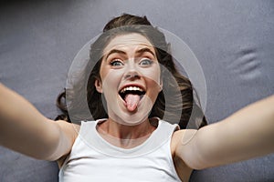Image of amusing woman showing her tongue and taking selfie photo
