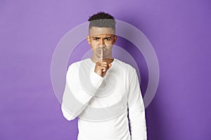 Image of angry african-american man hushing at you, press finger over lips, showing taboo sign, standing disappointed