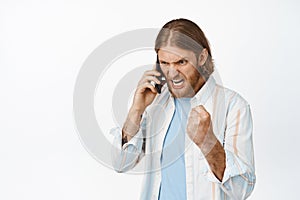 Image of angry blond bearded man cursing on phone call, screaming during conversation on mobile, shouting upset