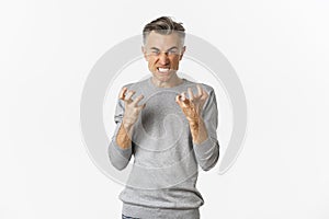 Image of angry middle-aged man cursing someone, looking mad and clenching fists with hatred, standing over white