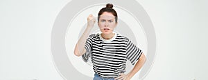 Image of angry woman threatening, shaking fist with disapproval, scolding someone, standing over white background