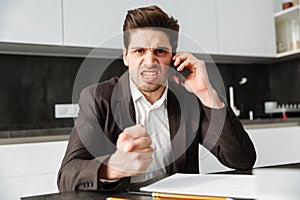 Angry young businessman talking by mobile phone.