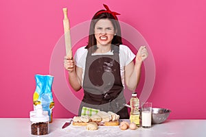 Image of annoyed angry housewife wearing dirty brown apron, white t shirt and red headband, being irritated, having unpleasant