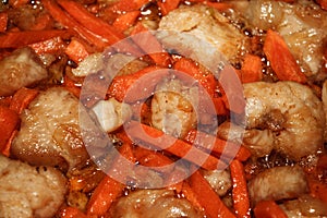 Image of appetizing fried chicken pieces with bright orange carrots with onion pieces in sunflower oil