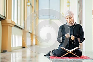 The image of an Asian Muslim woman in the Islamic religion in hijab in cream and black color. reading the Quran