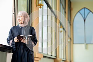 The image of an Asian Muslim woman in the Islamic religion in hijab in cream and black color. reading the Quran