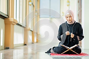 The image of an Asian Muslim woman in the Islamic religion in hijab in cream and black color. reading the Quran