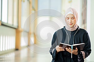 The image of an Asian Muslim woman in the Islamic religion in hijab in cream and black color. reading the Quran