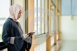 The image of an Asian Muslim woman in the Islamic religion in hijab in cream and black color. reading the Quran