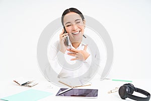 Image of asian woman in office, talks on cellphone, discuss work with client on mobile phone, sits over white background