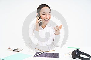 Image of asian woman in office, talks on cellphone, discuss work with client on mobile phone, sits over white background