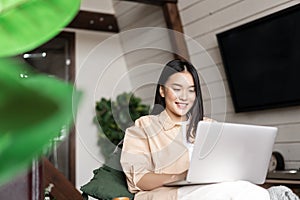 Image of asian woman working on laptop from cozy living room. Girl studying doing homework at home