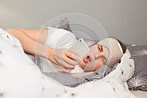 Image of astonished surprised woman in bed with sleep mask wakes up and looking at mobile display, sees unexpected news on a