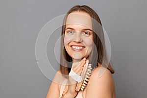 Image of attractive beautiful woman uses dry body brush wants to have smooth clean skin, massaging her shoulder and arm, looking