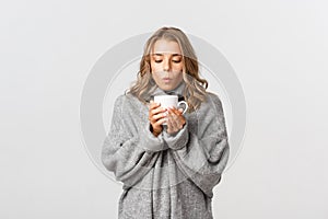 Image of attractive blond girl drinking hot tea or coffee, standing over white background