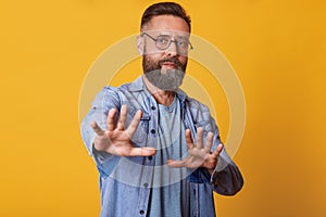 Image of attractive middle aged man showing refusal gesture, has serious facial expression, wearing stylish denim jacket, gray t