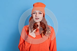 Image of attractive open mouth lady direct finger own chest, wear casual orange shirt and hat  blue color background,