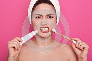 Image of attractive woman with dark hair, holding toothbrushe and tooth paste in hands, has angry facial expression, female