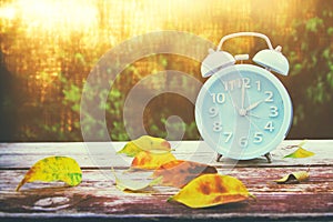 Image of autumn Time Change. Fall back concept. Dry leaves and vintage alarm Clock