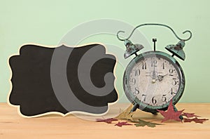 Image of autumn Time Change. Fall back concept. Dry leaves and vintage alarm Clock on rustic wooden table.