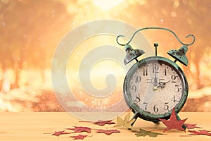 Image of autumn Time Change. Fall back concept. Dry leaves and vintage alarm Clock on rustic wooden table.