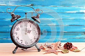 Image of autumn Time Change. Fall back concept. Dry leaves and vintage alarm Clock on rustic wooden table