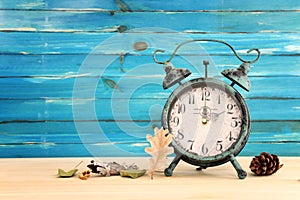 Image of autumn Time Change. Fall back concept. Dry leaves and vintage alarm Clock on rustic wooden table