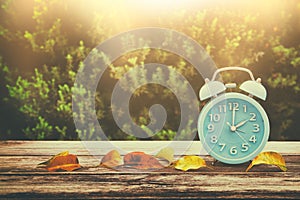 Image of autumn Time Change. Fall back concept. Dry leaves and vintage alarm Clock on wooden table