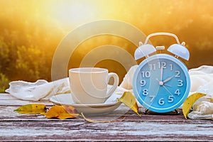 Image of autumn Time Change. Fall back concept. Dry leaves and vintage alarm Clock on wooden table outdoors at afternoon