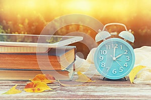 Image of autumn Time Change. Fall back concept. Dry leaves and vintage alarm Clock on wooden table outdoors at afternoon