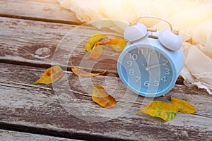 Image of autumn Time Change. Fall back concept. Dry leaves and vintage alarm Clock on wooden table outdoors at afternoon