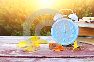 Image of autumn Time Change. Fall back concept. Dry leaves and vintage alarm Clock on wooden table