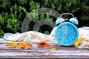 Image of autumn Time Change. Fall back concept. Dry leaves and vintage alarm Clock on wooden table