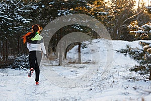 Image from back of athlete in sneakers on morning run against background of trees in winter