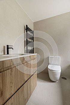 Image of the bathroom with cream-colored tiles, matching countertop, wooden cabinet with drawers and matching black taps with