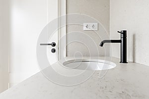 Image of the bathroom with cream tiles, matching countertop, matching black faucets with white door handle