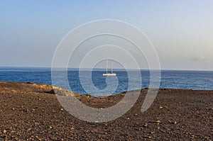 Image of a beach with a sailboat crossing the horizon