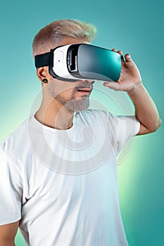 Image of bearded hipster man with blonde hair wearing virtual reality goggles in studio in neon lights.